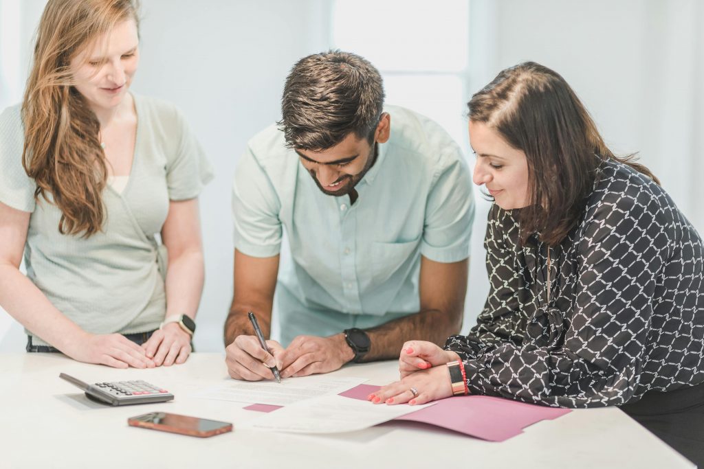 Three adults reviewing and signing real estate documents indoors.